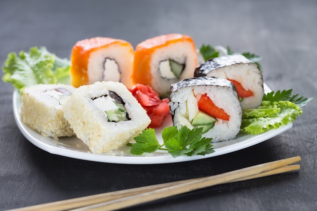 Sushi on a square white plate with parsley greens with sticks in the foreground. Gray 