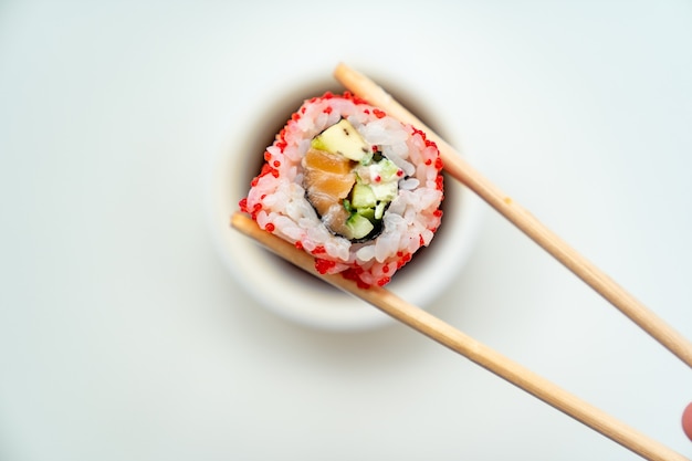 I bastoncini di sushi continuano a rotolare con una tazza di salsa di soia su sfondo bianco