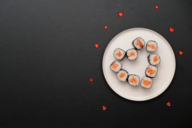 Sushi for Valentines Day - roll in heart shape, on plate on black background. Space for text.