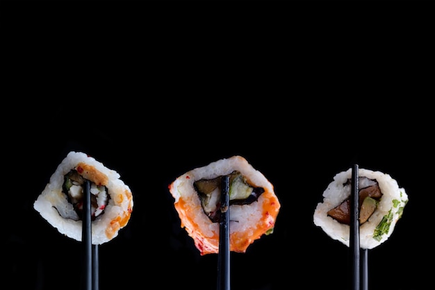 Sushi with black chopsticks on black background