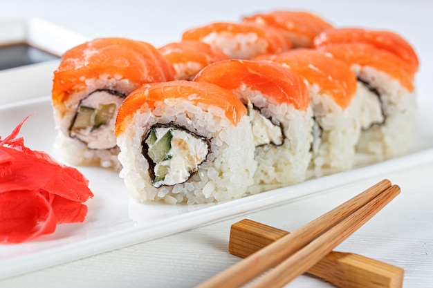 Sushi with salmon on a white plate with wasabi ginger soy chopsticks on a white background