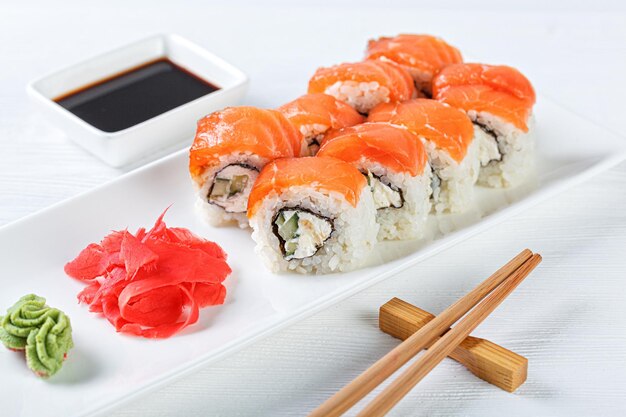 Sushi with salmon on a white plate with wasabi ginger soy chopsticks on a white background