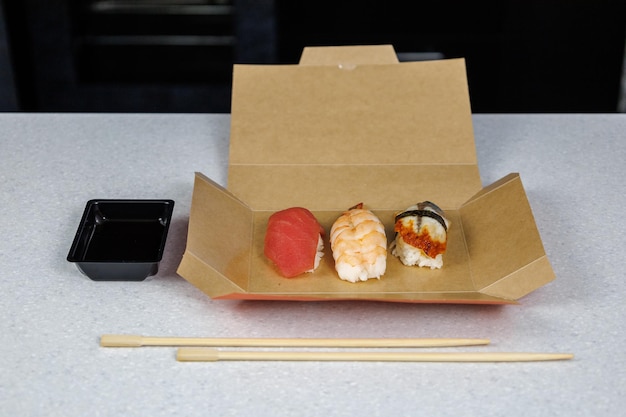 Sushi with tuna shrimp and eel lies in a cardboard box on the table in the kitchen Fast food concept