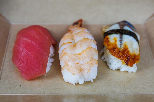 Sushi with tuna shrimp and eel lies in a cardboard box on the table in the kitchen Fast food concept