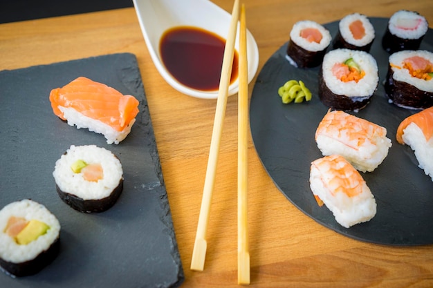 Sushi on a wooden table on black slate plate with soy sauce and chopsticks