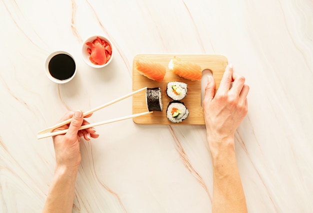 Sushi zalm ingesteld op houten snijplank. Vrouw hand met sushi roll met chipsticks. Plat leggen