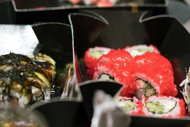 Sushibroodjes met kleine rode kaviaar rond de broodjes in een zwarte verpakking Menu-elementen Dineren Exotische voeding Voeding Voeden Levensmiddelen Bereid cilindrische keuken Serveren