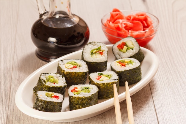 Sushibroodjes met rijststukjes van avocado, komkommer, rode paprika en slablaadjes op keramische plaat