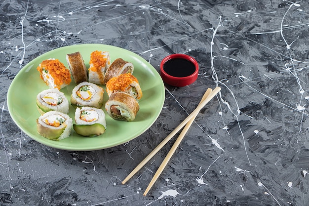 Sushibroodjes met sojasaus op een groene plaat met stokjes geplaatst.