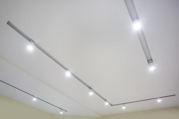 Suspended ceiling with halogen spots lamps and drywall\
construction in empty room in apartment or house stretch ceiling\
white and complex shape
