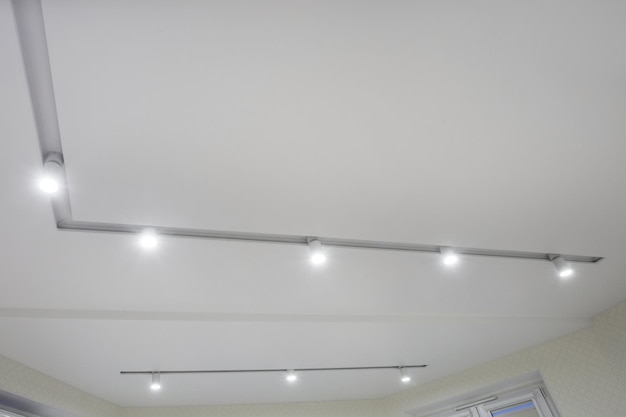 Suspended ceiling with halogen spots lamps and drywall\
construction in empty room in apartment or house stretch ceiling\
white and complex shape