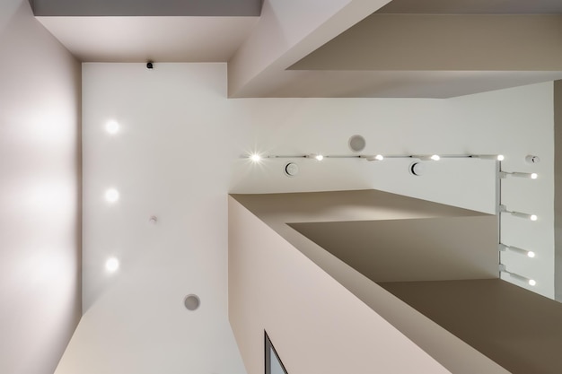 Suspended ceiling with halogen spots lamps and drywall\
construction in empty room in apartment or house stretch ceiling\
white and complex shape