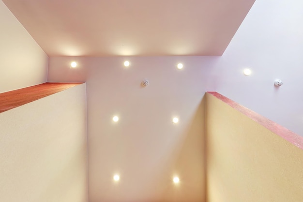 Soffitto sospeso con lampade alogene e costruzione in cartongesso in una stanza vuota in appartamento o casa soffitto teso bianco e di forma complessa