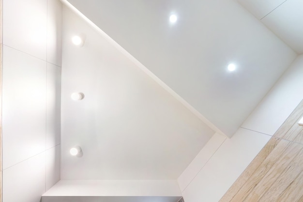 Suspended ceiling with led lightspot lamps and drywall\
construction in empty room in apartment or house stretch ceiling\
white and complex shape looking up