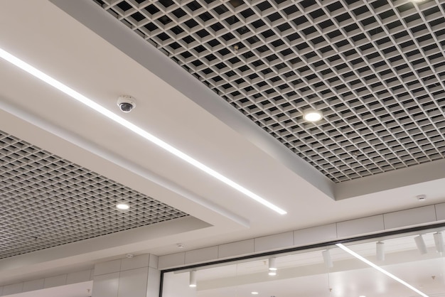 Подвесной и сетчатый потолок с галогенными точечными лампами и гипсокартонной конструкцией в пустой комнате в магазине или доме. Натяжной потолок белого цвета и сложной формы.