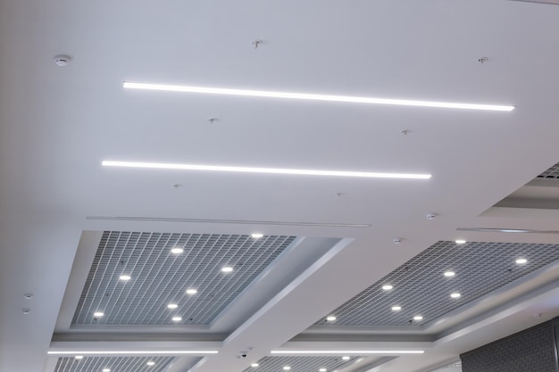 Suspended and grid ceiling with halogen spots lamps and drywall
construction in empty room in store or house stretch ceiling white
and complex shape