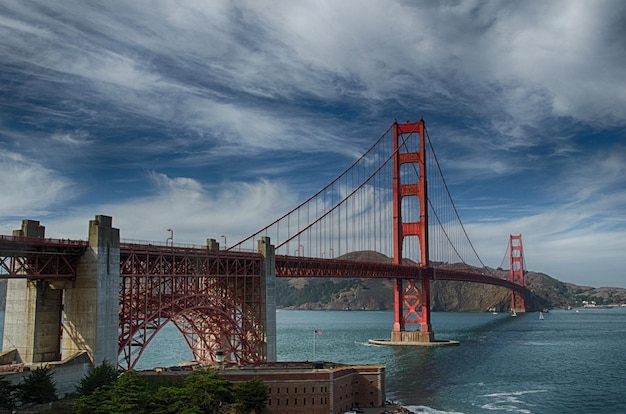 Suspension bridge over river against cloudy sky