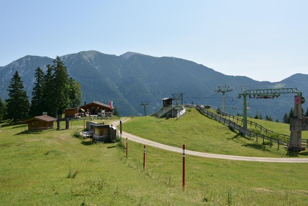 緑の草と木造の家で覆われた山の斜面の背景に吊り吊りケーブルカー