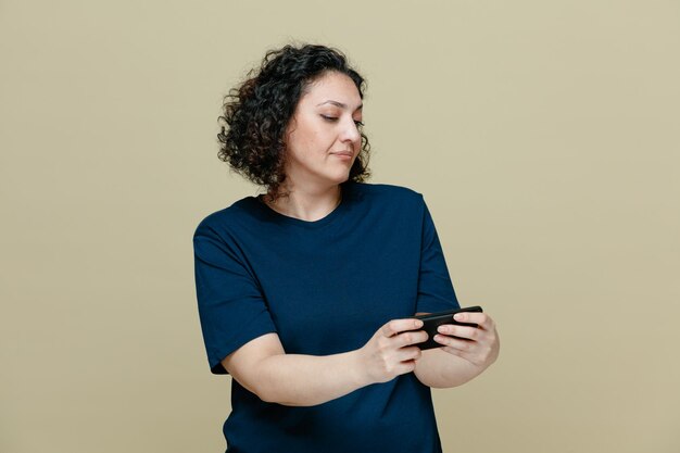 Suspicious middleaged woman wearing tshirt using her mobile phone isolated on olive green background