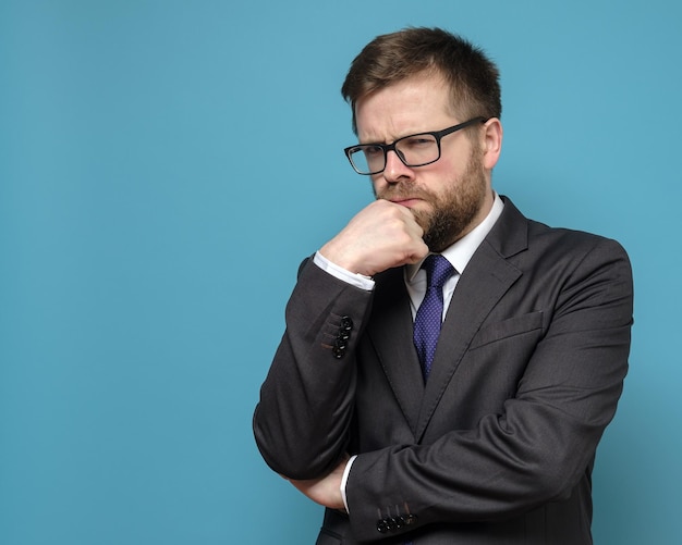 Suspicious pensive business man in a suit and glasses looks sternly holding hand to his face