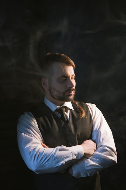 Suspicious stylish adult man. Fashion backdrop. Handsome thoughtful male in smart clothes on black background with backlight with smoke. Business worker closeup, style concept