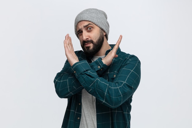 Suspicious young man wearing winter hat looking at camera showing no gesture isolated on white background