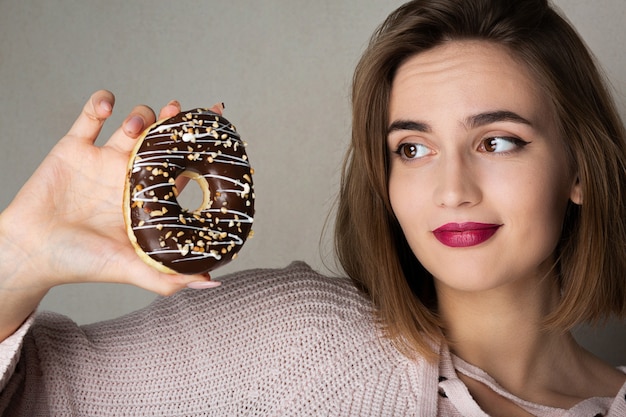 Suspicious young model holding donut against a grey background. Space for text