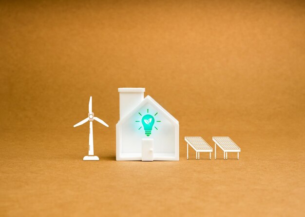 Фото Устойчивость в домашней концепции зеленая листья лампочка в небольшом белом игрушечном доме украшение с солнечными панелями и символом ветряной мельницы на коричневом фоне переработанной бумаги минимальная экологически чистая технология