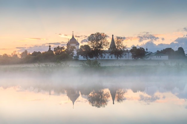 Suzdal town in Russia. Beautiful summer landscape at foggy sunrise. Nativity Cathedral and trees are reflected in the river.