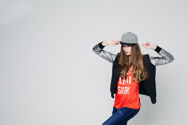 Swag stylish teenage girl in cap posing with hands up.