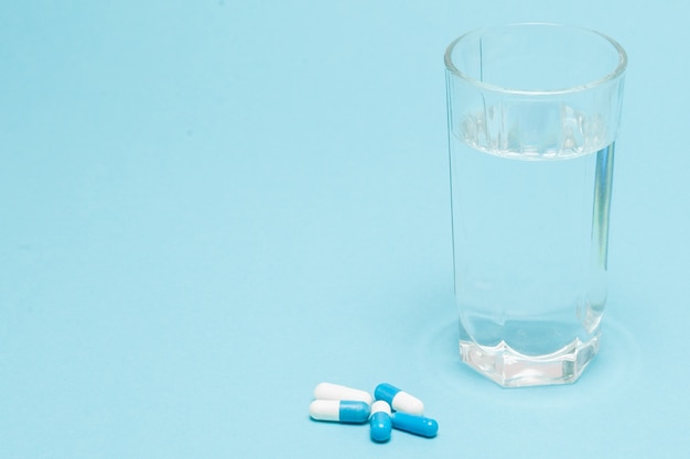 Swallowing tablets. Pills and a glass of water against a blue table background. Top view, copy space, flat lay.