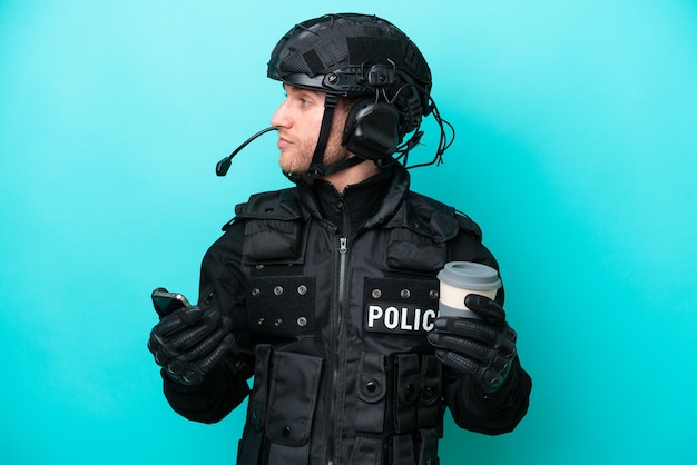 SWAT blanke man geïsoleerd op blauwe achtergrond met koffie om mee te nemen en een mobiel