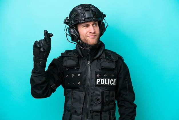 SWAT caucasian man isolated on blue background with fingers crossing and wishing the best