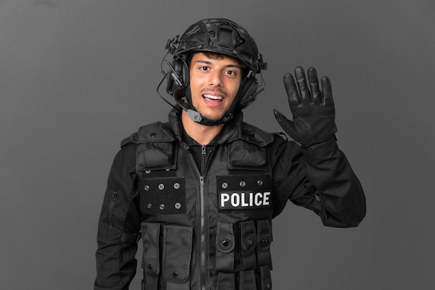 SWAT caucasian man isolated on grey background saluting with hand with happy expression