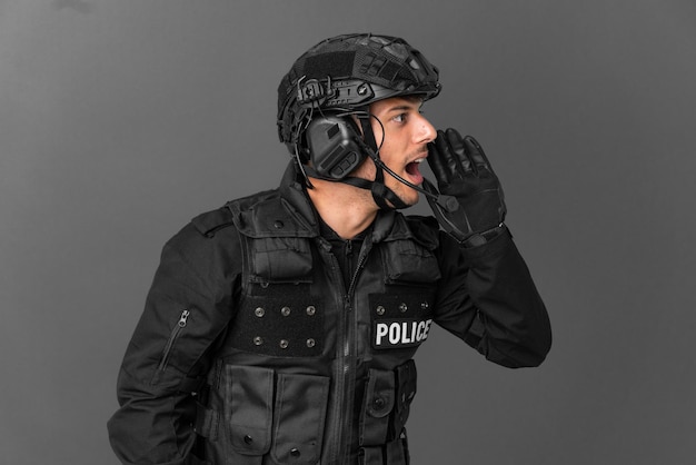 SWAT caucasian man isolated on grey background shouting with mouth wide open to the lateral