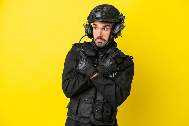 SWAT caucasian man isolated on yellow background pointing to the laterals having doubts