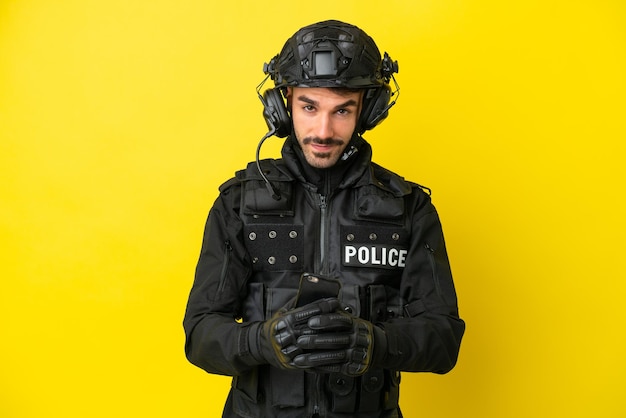 Кавказский мужчина SWAT изолирован на желтом фоне, отправляя сообщение с мобильного телефона