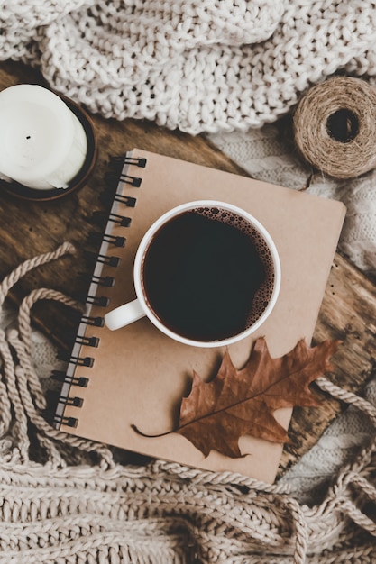 Sweaters and cup of tea with notebook, candle and knitting clothes