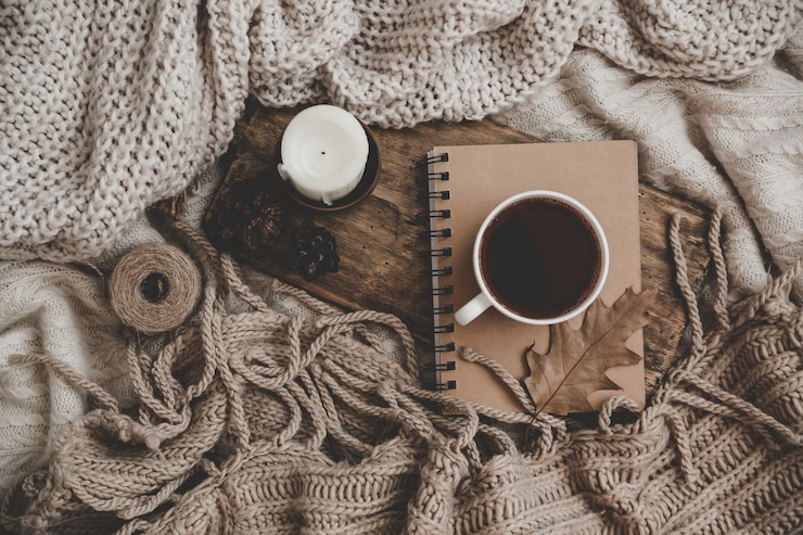 Photo sweaters and cup of tea with notebook, candle and knitting clothes