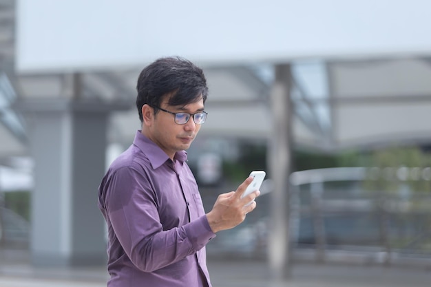 Sweating young asian businessman looking at messages on cellphone while walking in the street.