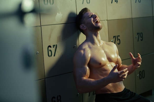 Sweaty sportsman in despair shouting with his eyes closed in locker room after exhausting sports training