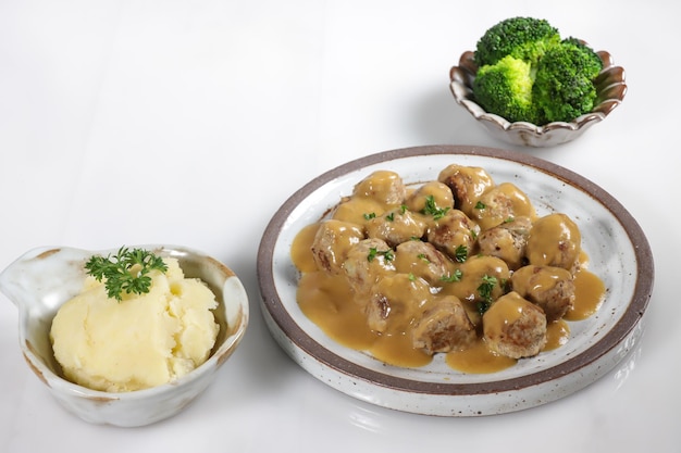 Swedish Meatball with brown mushroom sauce. Served on ceramic plate, on white table.