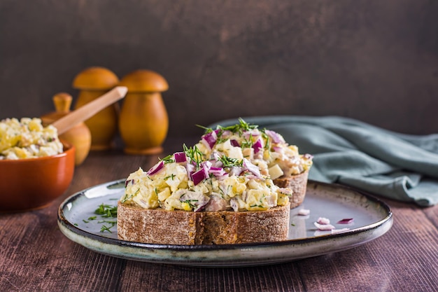 Шведский салат с анчоусами, картофелем и яйцом на ржаном хлебе на тарелке