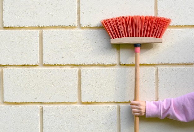 sweeping brush with red bristles in a woman's hand near a brick wall