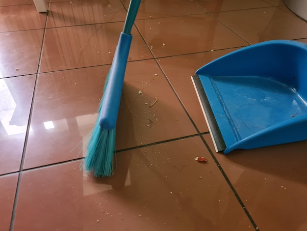Sweeping dust with a blue broom on tiled floor