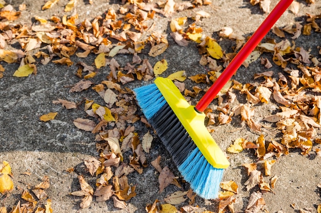 Sweeping the fallen leaves from the garden ground for recycling during autumn fall season.Man brooming the street to collect dry fallen leaves.