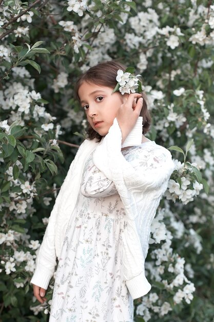 A sweet 9yearold girl with big beautiful eyes and a light dress in blooming white apple trees Spring walks in the blooming garden apple blossom