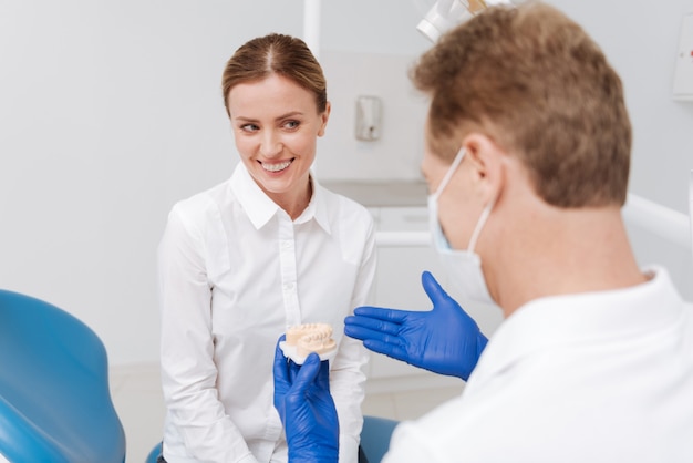 Dolce adorabile donna graziosa che riceve un'utile lezione sull'igiene dentale mentre paga una visita al suo dentista e chiede la sua consulenza