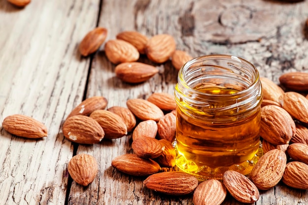 Sweet Almond Oil first extraction in a small glass jar dry almond nuts on an old wooden background selective focus