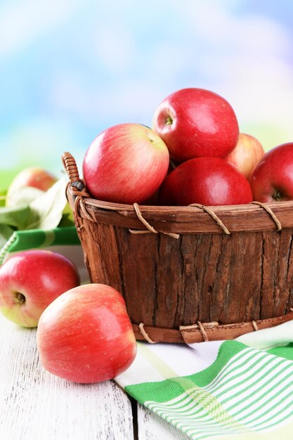 Sweet apples in wooden basket on table on bright background